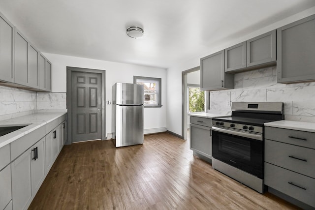 kitchen with gray cabinetry, sink, decorative backsplash, appliances with stainless steel finishes, and hardwood / wood-style flooring