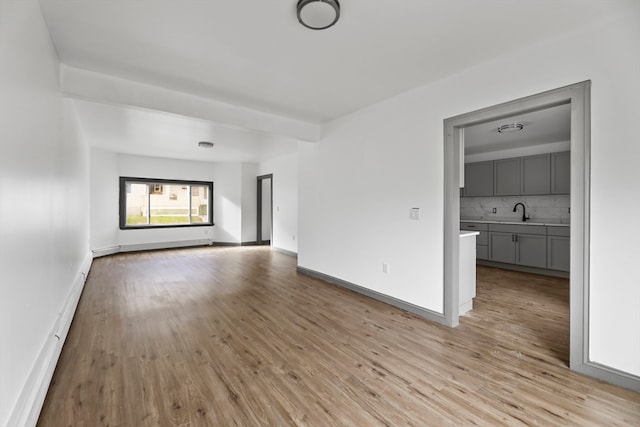 empty room featuring beamed ceiling, light hardwood / wood-style floors, and sink