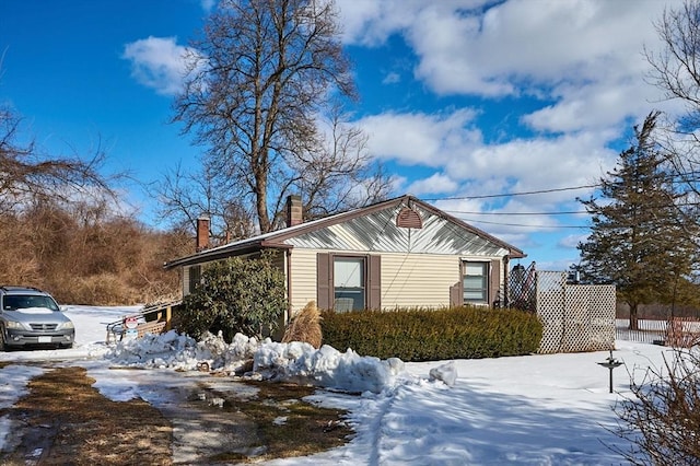 view of snow covered exterior with a chimney and fence