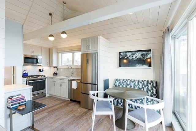 kitchen with wood walls, sink, lofted ceiling with beams, light hardwood / wood-style floors, and stainless steel appliances