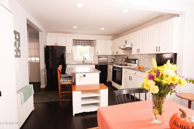 kitchen with radiator heating unit, sink, white cabinetry, a center island, and black appliances