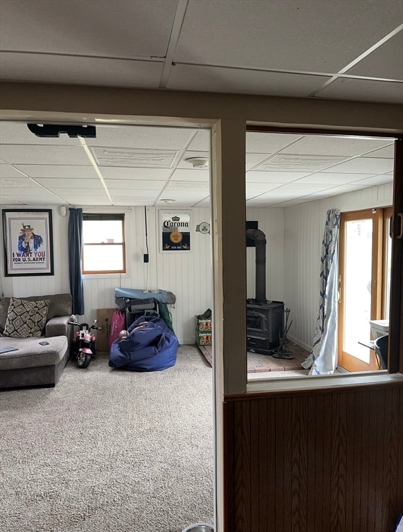 basement with a wood stove, wooden walls, a drop ceiling, and carpet floors