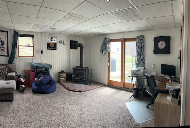 living room featuring carpet, a drop ceiling, and a wood stove