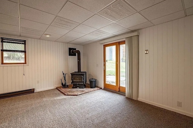 unfurnished living room featuring carpet floors, a wood stove, a drop ceiling, and wooden walls