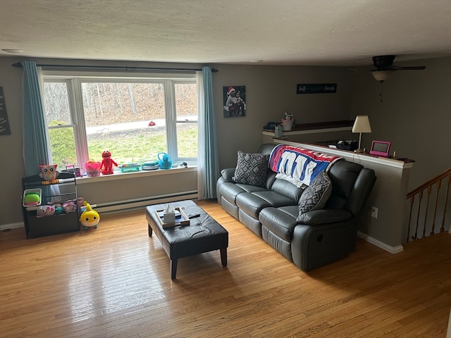 living room with a textured ceiling, light hardwood / wood-style floors, baseboard heating, and ceiling fan