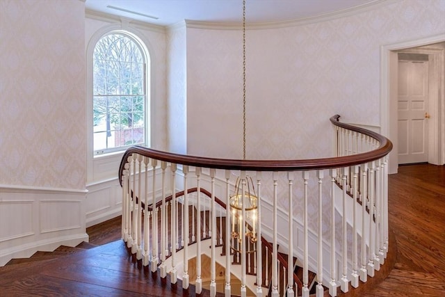 staircase featuring wallpapered walls, wood finished floors, crown molding, a decorative wall, and wainscoting