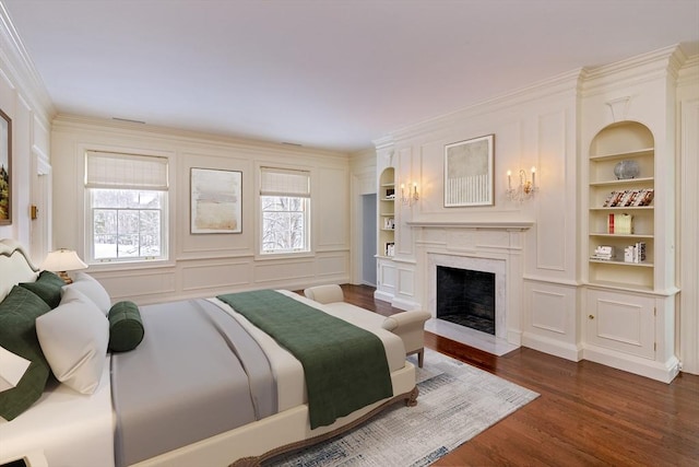 bedroom with crown molding, a decorative wall, dark wood-style floors, and a high end fireplace