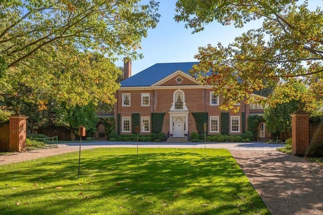 colonial inspired home with a front lawn, brick siding, driveway, and a chimney