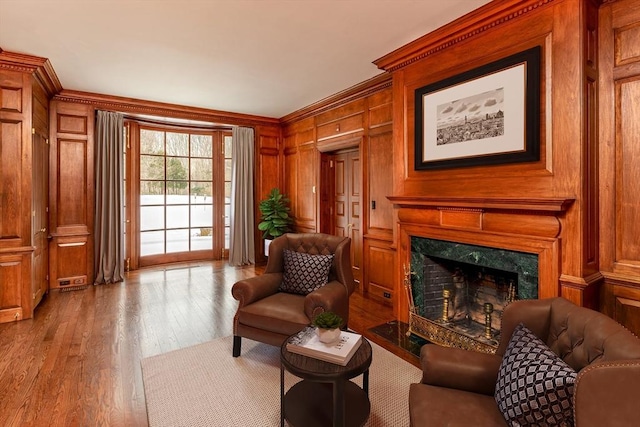 living area with a premium fireplace, wooden walls, wood finished floors, and crown molding