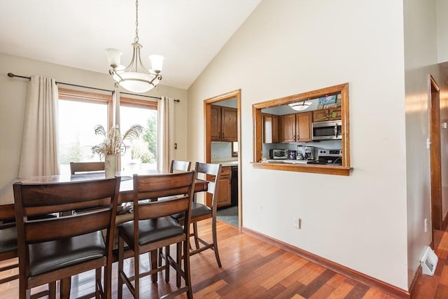 dining room with a chandelier, light wood-style flooring, baseboards, and high vaulted ceiling