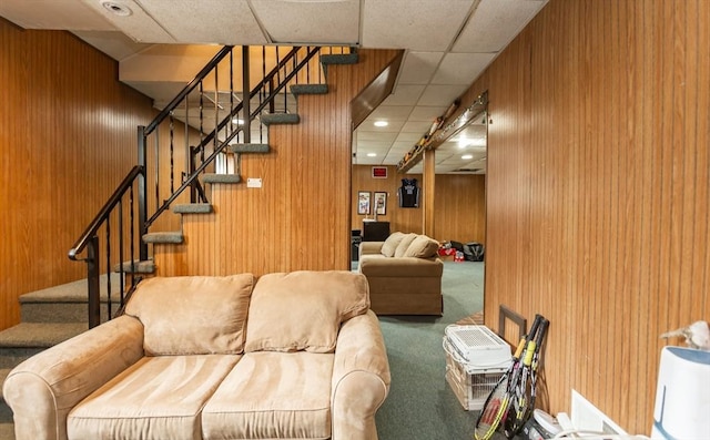 living room with stairway, carpet, wooden walls, a drop ceiling, and recessed lighting
