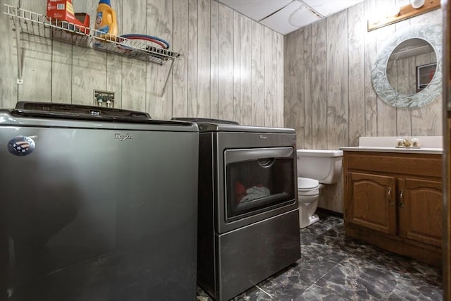 laundry area with washer and dryer, wood walls, and dark marble finish flooring