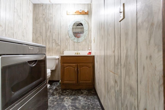 half bathroom featuring wooden walls, toilet, and vanity