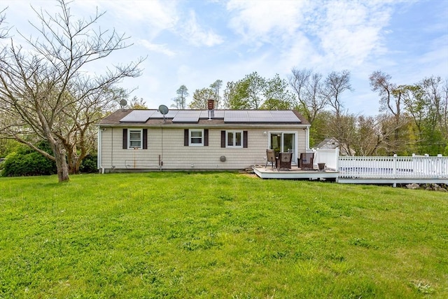back of property featuring a wooden deck, solar panels, a lawn, and a chimney