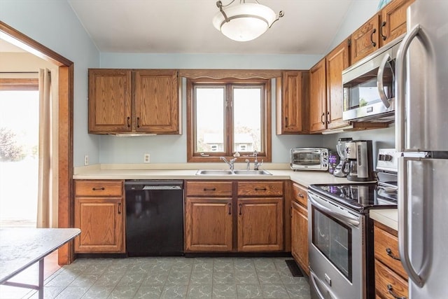 kitchen featuring stainless steel appliances, a sink, brown cabinetry, plenty of natural light, and vaulted ceiling