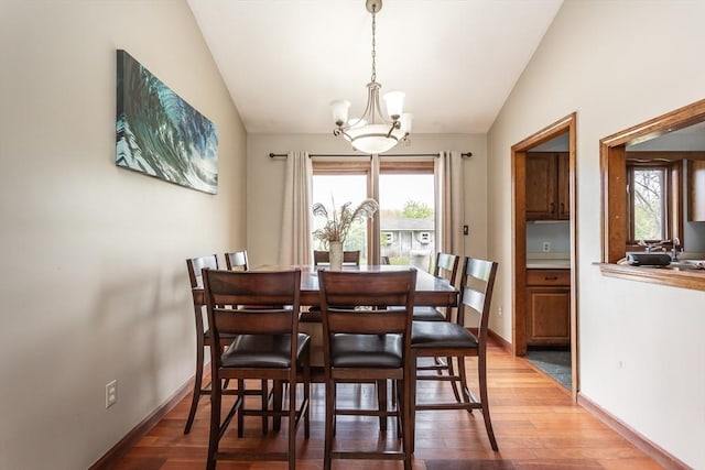 dining space with vaulted ceiling, a chandelier, light wood finished floors, plenty of natural light, and baseboards