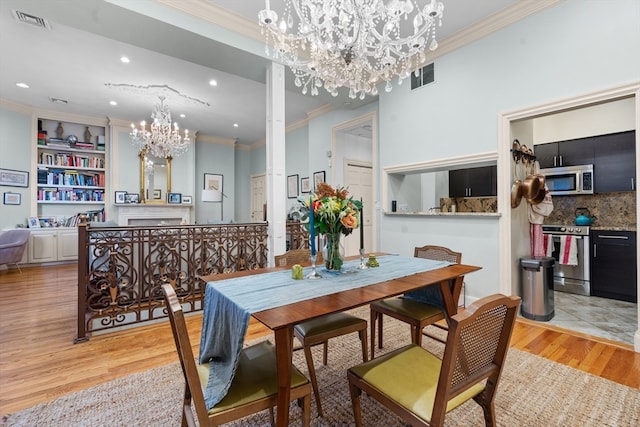 dining room with ornate columns, light wood-type flooring, crown molding, an inviting chandelier, and built in features