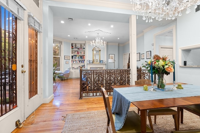 dining room featuring light wood-type flooring, ornamental molding, a chandelier, and built in features