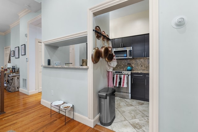 kitchen featuring light stone counters, light hardwood / wood-style flooring, appliances with stainless steel finishes, crown molding, and decorative backsplash