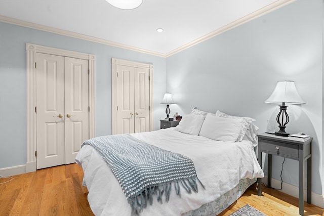 bedroom featuring light wood-type flooring, ornamental molding, and two closets