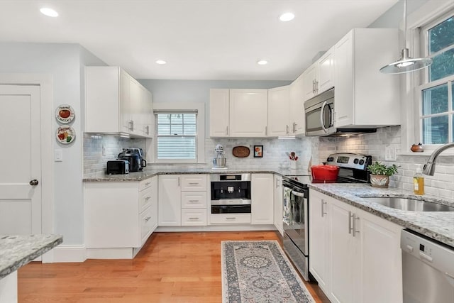 kitchen with appliances with stainless steel finishes, a sink, light wood-style flooring, white cabinets, and recessed lighting