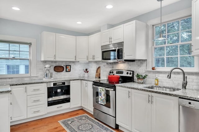 kitchen featuring appliances with stainless steel finishes, a sink, white cabinetry, tasteful backsplash, and light stone countertops
