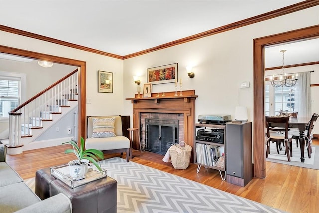 living area featuring a chandelier, stairs, wood finished floors, a fireplace, and crown molding