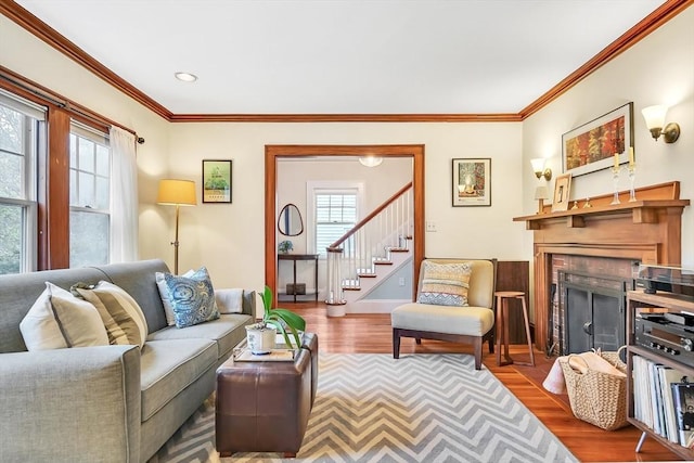 living room with wood finished floors, healthy amount of natural light, a fireplace with flush hearth, stairs, and ornamental molding