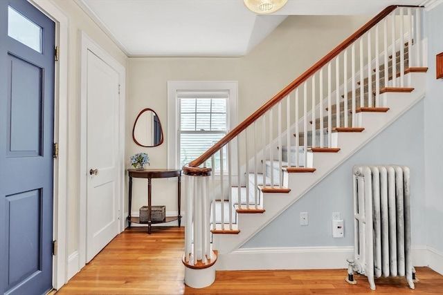 stairway with radiator, wood finished floors, and baseboards