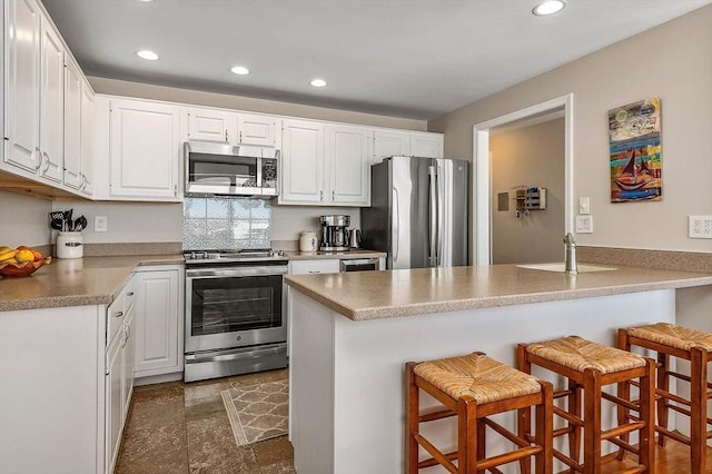 kitchen featuring a breakfast bar, a sink, stainless steel appliances, recessed lighting, and a peninsula