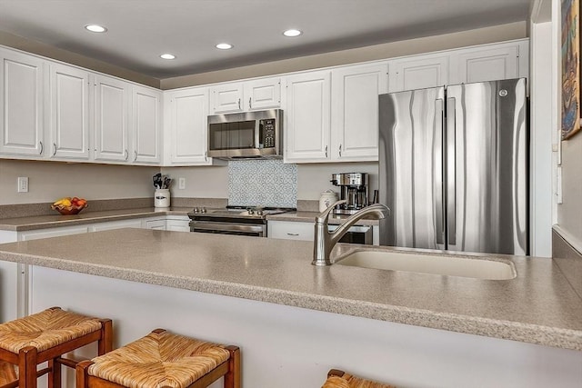 kitchen featuring white cabinets, appliances with stainless steel finishes, a sink, a kitchen breakfast bar, and recessed lighting
