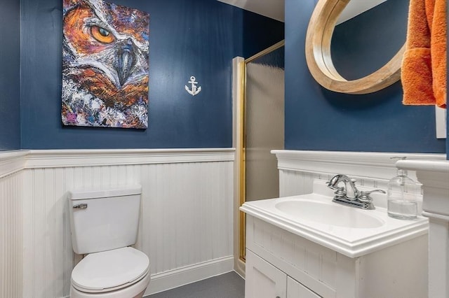 bathroom with vanity, a shower with shower door, wainscoting, and toilet