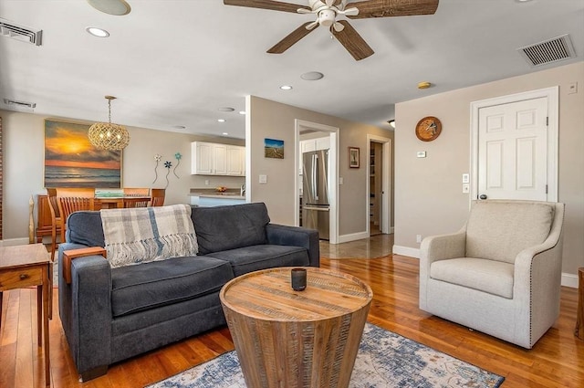 living room with visible vents, light wood-style floors, and ceiling fan with notable chandelier