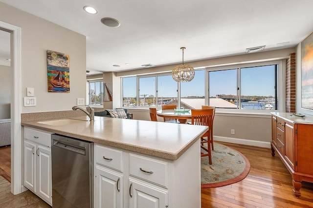 kitchen featuring stainless steel dishwasher, a peninsula, white cabinets, a sink, and light wood-style flooring