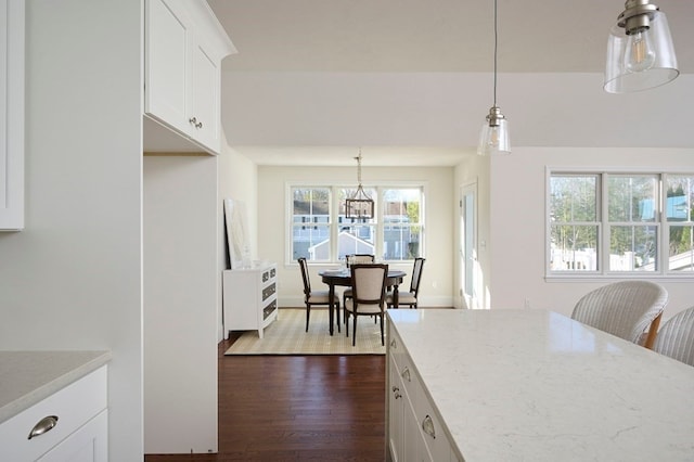 kitchen with white cabinets, wood-type flooring, pendant lighting, and light stone counters