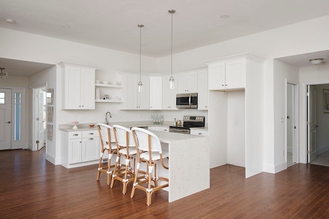 kitchen with white cabinetry, a breakfast bar area, dark wood-type flooring, hanging light fixtures, and stainless steel appliances