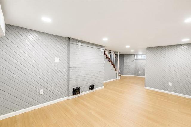 finished below grade area with baseboards, light wood-style floors, stairs, recessed lighting, and wooden walls