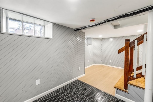 below grade area featuring wooden walls, wood finished floors, baseboards, and stairway