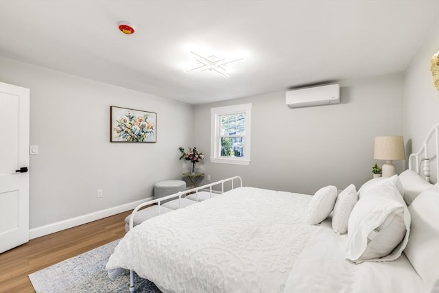 bedroom with an AC wall unit, wood finished floors, and baseboards