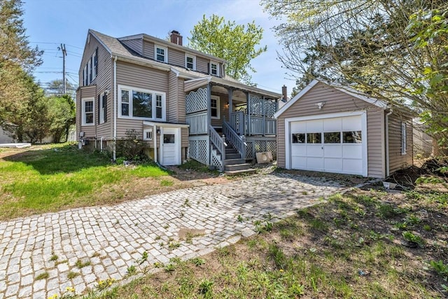 view of front of home with a detached garage, a porch, an outdoor structure, decorative driveway, and a chimney