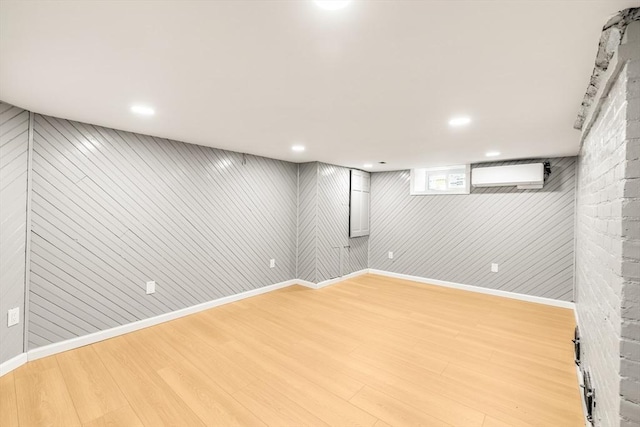 below grade area featuring light wood-style floors, a wall mounted AC, baseboards, recessed lighting, and wooden walls