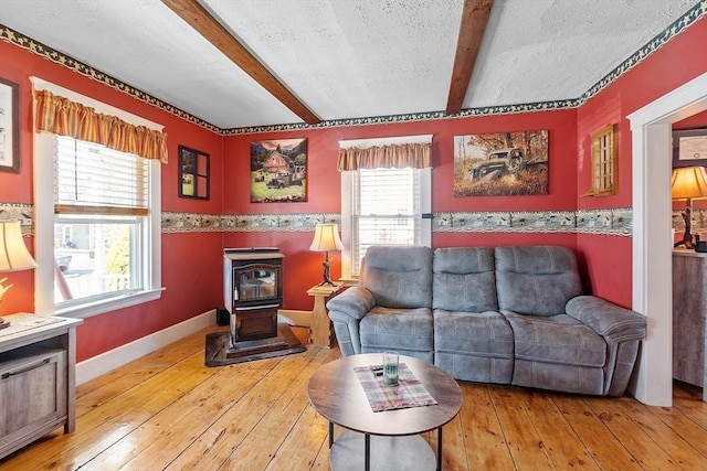 living room featuring a textured ceiling, hardwood / wood-style flooring, beam ceiling, and a wood stove