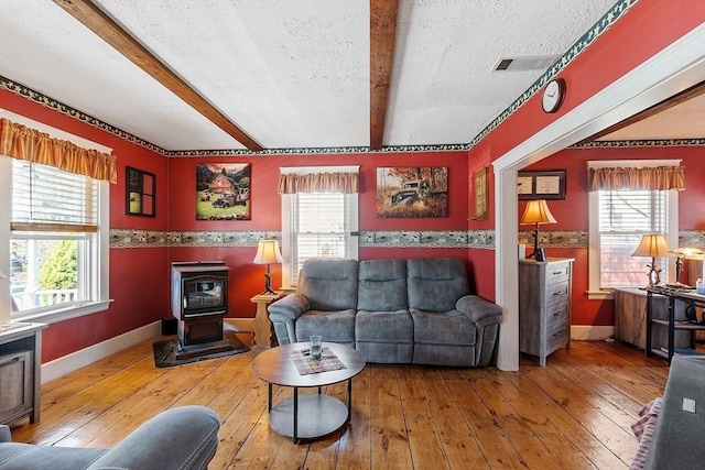 living area with wood-type flooring, beamed ceiling, baseboards, and a wood stove