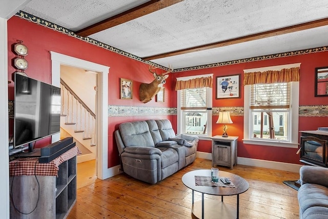 living room with a wood stove, a textured ceiling, stairs, beamed ceiling, and hardwood / wood-style flooring