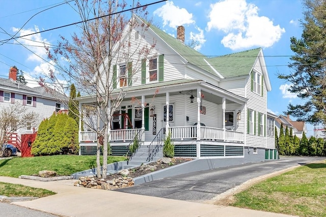 view of front of home featuring covered porch, a chimney, and a front yard