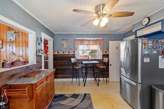 kitchen with brown cabinetry, light floors, ceiling fan, wooden walls, and stainless steel fridge