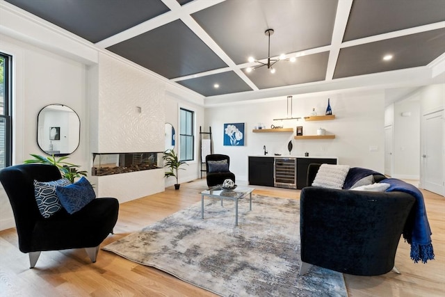 living room with coffered ceiling, a multi sided fireplace, wine cooler, a notable chandelier, and light hardwood / wood-style floors