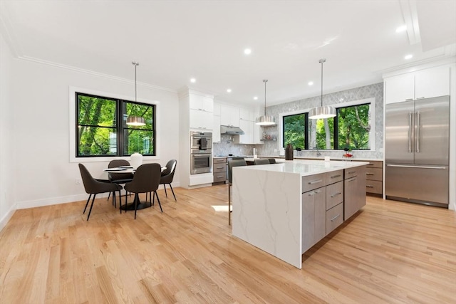 kitchen featuring white cabinets, a spacious island, hanging light fixtures, light stone counters, and stainless steel appliances