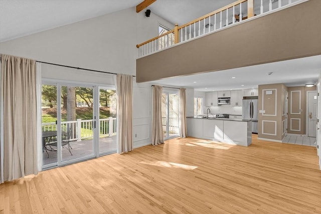 unfurnished living room featuring beam ceiling, light wood-style floors, high vaulted ceiling, recessed lighting, and a sink