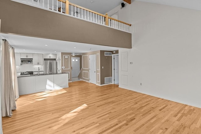 unfurnished living room with light wood-style floors, high vaulted ceiling, baseboards, and visible vents